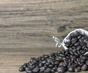 A selective focus shot of coffee beans spilling out the bag on a wooden surface